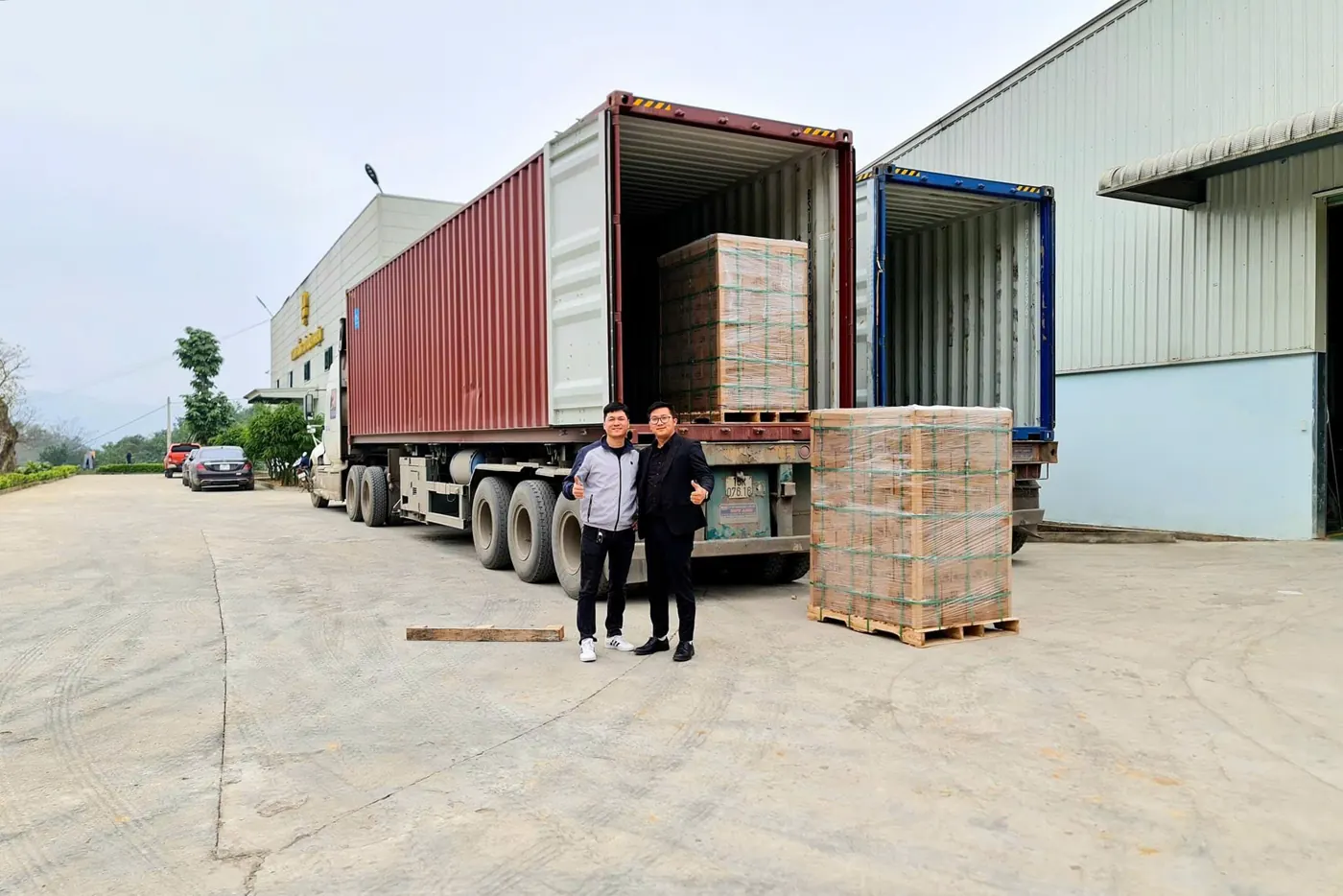 Khánh và Xuân đứng trước hai container đang xếp hàng rượu 9 Chum xuất khẩu tại sân nhà máy